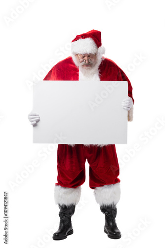 Smiling Santa Claus standing up on white background holding and looking down on a blank white sign for Christmas holiday advertising ad or copy space