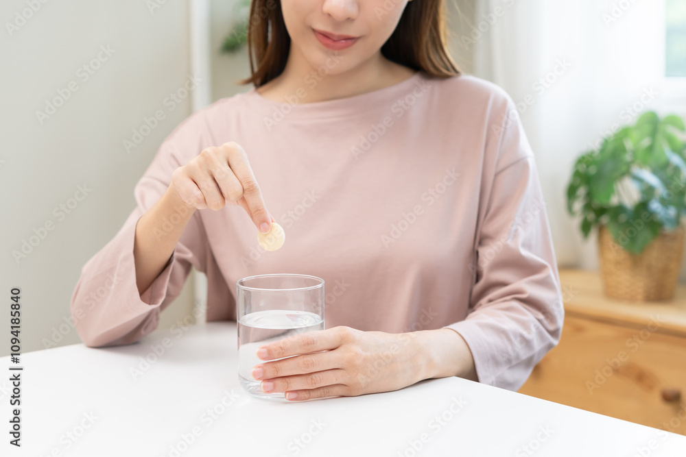 Smile asian young woman putting or dropping effervescent tablet into glass of water, holding pain pill, painkiller medicine, aspirin for treatment, take vitamin c for hangover. Health care concept. Smile asian young woman putting or dropping effervescent tablet into glass of water, holding pain pill, painkiller medicine, aspirin for treatment, take vitamin c for hangover. Health care concept.