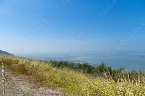 Viewpoint with ground and grass growing on the green edge. View of Lam Takhong Reservoir and the distant blurry mountain range.