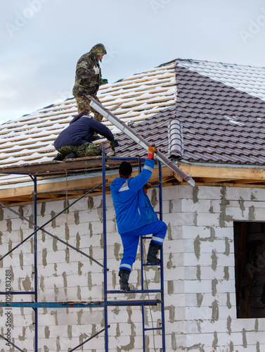 Three men are working on a roof, one of them is wearing a blue jacket