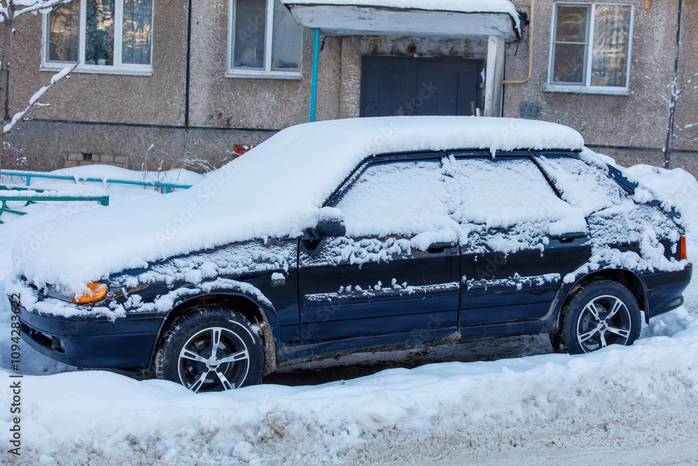 A black car covered in snow sits on a snowy road