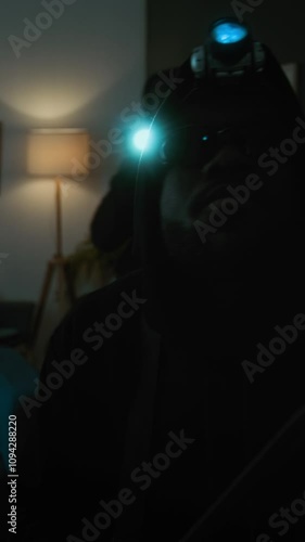 Vertical view of thief with headlamp holding crowbar glancing around living room, his accomplice with flashlight in background photo