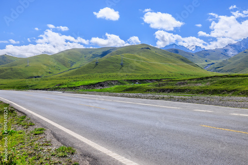 Countryside asphalt road and green meadow with mountains nature landscape in Xinjiang, China. Road trip.