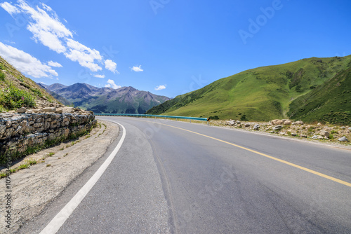 Countryside asphalt road and green meadow with mountains nature landscape on a sunny day. Road trip.