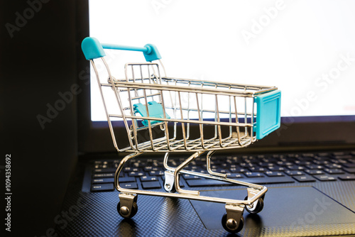 A decorative grocery cart sits on top of a laptop.
