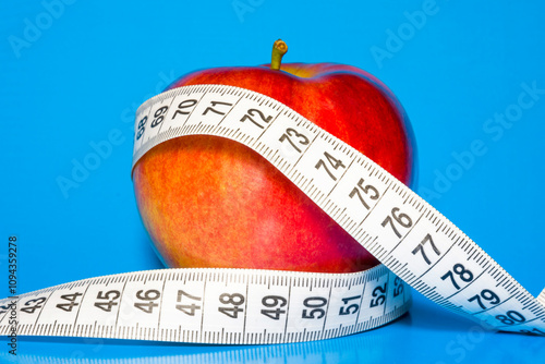 Red apple wrapped in measuring tape on blue background.