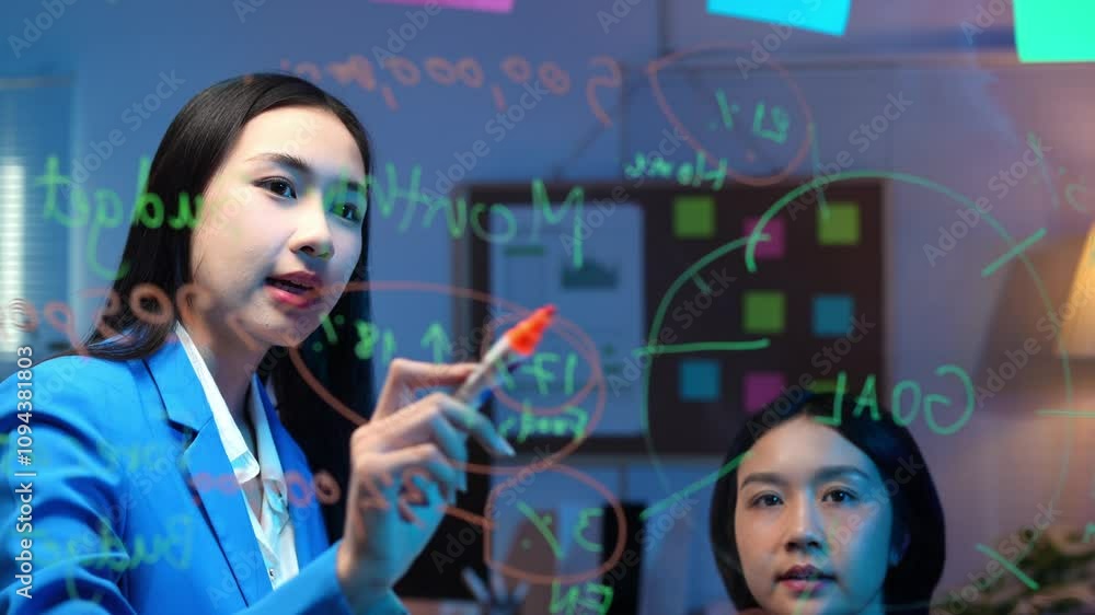 Two Asian businesswomen are meeting in office, modern, brainstorming, discussing, analyzing and writing plans on a glass board together in business, planning, performance summary, calculations. Two Asian businesswomen are meeting in office, modern, brainstorming, discussing, analyzing and writing plans on a glass board together in business, planning, performance summary, calculations.