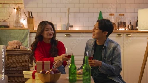 Slow motion young Asian couple having a small party in the kitchen, sipping wine and chatting together, enjoying a relaxed and intimate celebration.