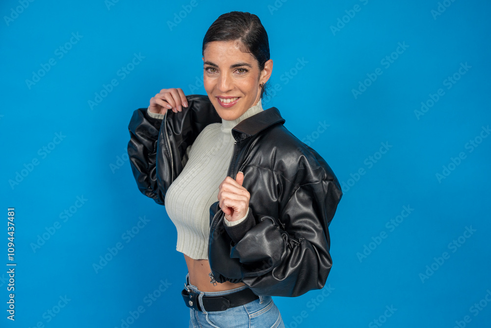 Naklejka premium Young woman wearing black leather jacket and smiling on blue background
