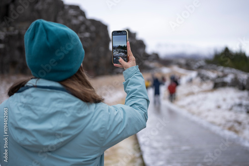 Mujer de espaldas haciendo foto y video con teléfono movil en paisaje con nieve con personas desenfocadas