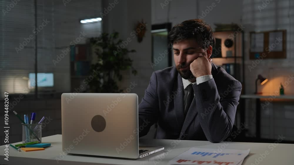 Adult business man manager sitting at desk working on laptop in office overtime in evening, typing doing research, reading data, tired bored expression. Adult business man manager sitting at desk working on laptop in office overtime in evening, typing doing research, reading data, tired bored expression.