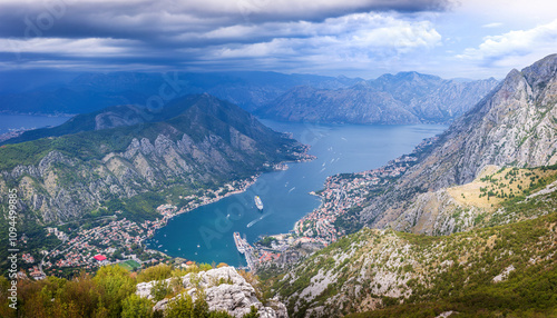 View of the Bay of Kotor, Montenegro, from a high mountain road with winding switchbacks. The scenic panorama includes the towns of Kotor and Tivat, and the Adriatic Sea.