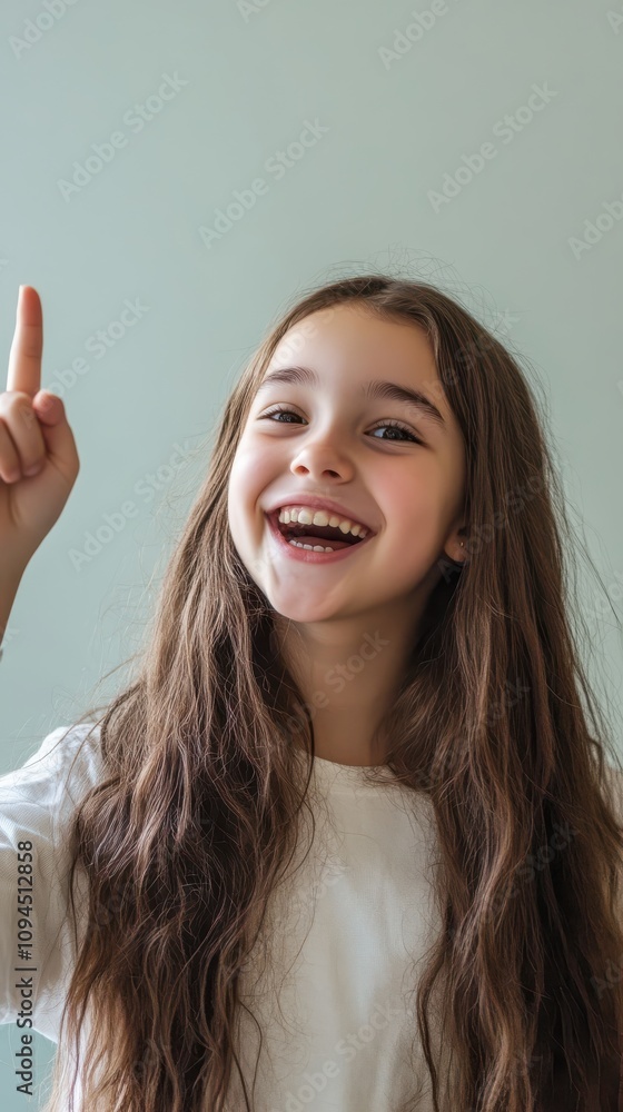 Cheerful young girl with long hair raising finger indoors joyfully Cheerful young girl with long hair raising finger indoors joyfully