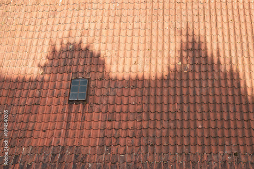 Old style red tiled roof with a small window and shadow.