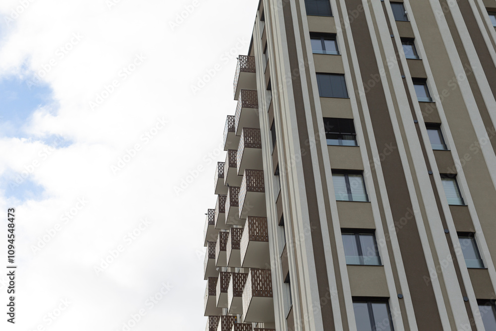 A tall highrise with balconies and windows, set against a cloudy sky, creates a captivating view A tall highrise with balconies and windows, set against a cloudy sky, creates a captivating view