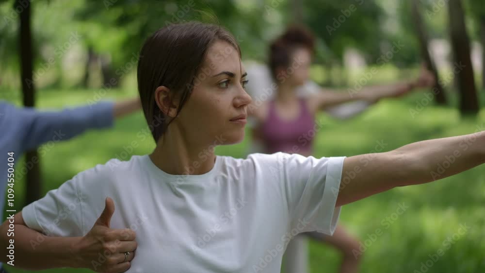 A yoga student in a white outfit practices the Warrior II pose during an outdoor session in a lush green park. The serene environment enhances focus and mindfulness as the group engages in their yoga A yoga student in a white outfit practices the Warrior II pose during an outdoor session in a lush green park. The serene environment enhances focus and mindfulness as the group engages in their yoga