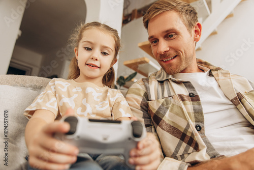 Portrait of happy, attractive man and his little daughter playing video games, holding joystick