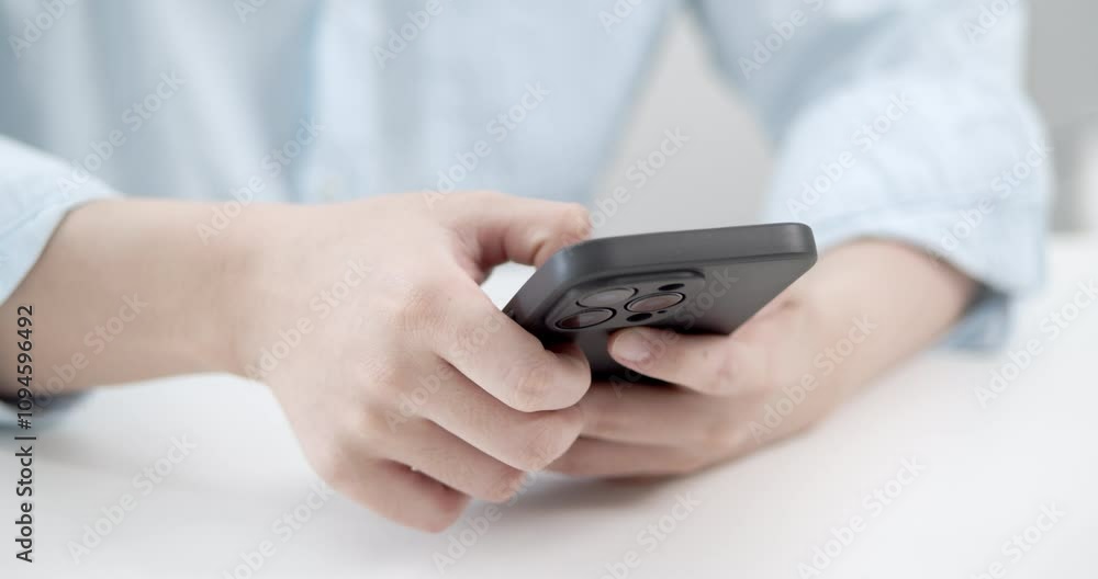 A person actively engages with their smartphone in a bright indoor space highlighting modern digital communication. A person actively engages with their smartphone in a bright indoor space highlighting modern digital communication.