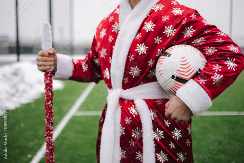 Close-up of Santa figure in a red robe with a soccer ball and staff, standing confidently on a green field. photo