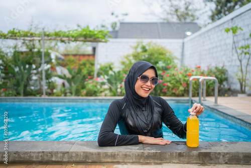 Tablou pe pânză An elegant woman in modest swimwear relaxes by the poolside with a refreshing dr
