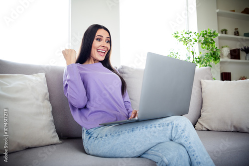 Happy young woman in stylish lavender pullover smiling with excitement while using a laptop at home during a leisurely weekend