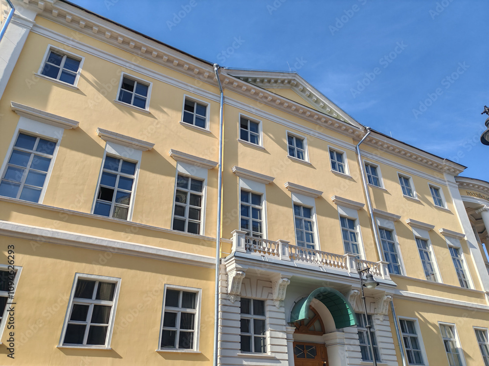grand yellow building with symmetrical windows and classical detailing, featuring a decorative arched entrance. The clean facade highlights the elegance of traditional urban architecture under a clear grand yellow building with symmetrical windows and classical detailing, featuring a decorative arched entrance. The clean facade highlights the elegance of traditional urban architecture under a clear