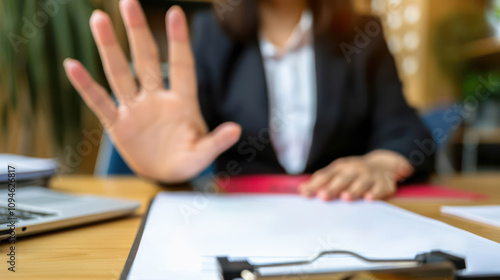 A person holding up their hand in refusal, symbolizing objection or rejection in a confident stance with Clipboard and Documents in Office
