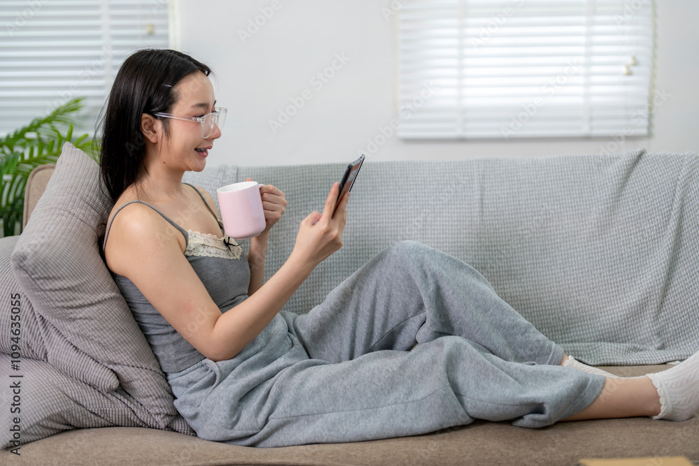 Young woman relaxing on sofa using smartphone and drinking coffee Young woman relaxing on sofa using smartphone and drinking coffee