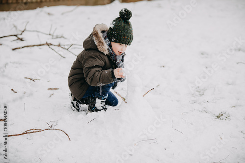 Bild auf Leinwand Child playing in snow crouching outdoors in winter clothing