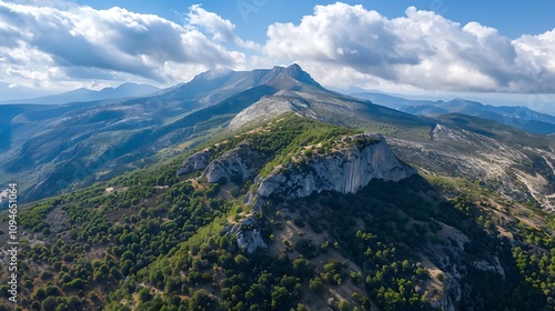 Aerial view of a mountainous landscape with lush greenery and dramatic clouds overhead.