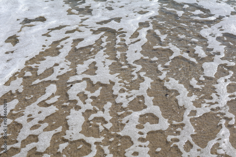 Obraz premium Close-up of intricate sea foam patterns on a sandy beach, showcasing the beauty of ocean textures.