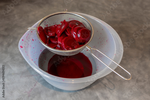Foto Straining Cooked Sliced Red Beetroot in Metal Strainer over Plastic Bowl on Wood