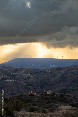 Wallpaper Mural A dramatic landscape featuring wind turbines on a distant mountain ridge, illuminated by sunset rays breaking through storm clouds. Environmental green electricity. Wind turbines, a wind farm Torontodigital.ca
