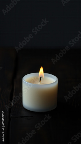 A lone white candle on a dark wooden table