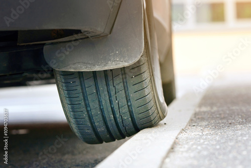 Parked car with one wheel on curb. Poor driving, incorrect parking. Wheel on curb, traffic violation. Car parked on curb, tire and wheel closeup. . photo