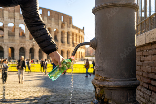 A person fills a bottle at a nasone, Rome's free public fountain, with the Colosseum in the background in Italy