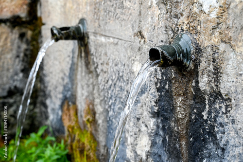 Spring drinking water pours from an iron pipe. Pure mountain water flows from the pipe. Clean spring water. Public fountain. 