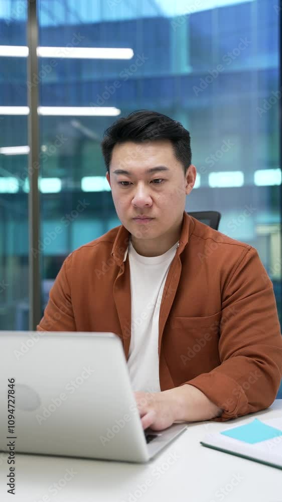 Confident Asian businessman typing on laptop sitting at workplace in business office. Male working in computer application, banking, texting client, chatting online. busy with project. Vertical video Confident Asian businessman typing on laptop sitting at workplace in business office. Male working in computer application, banking, texting client, chatting online. busy with project. Vertical video