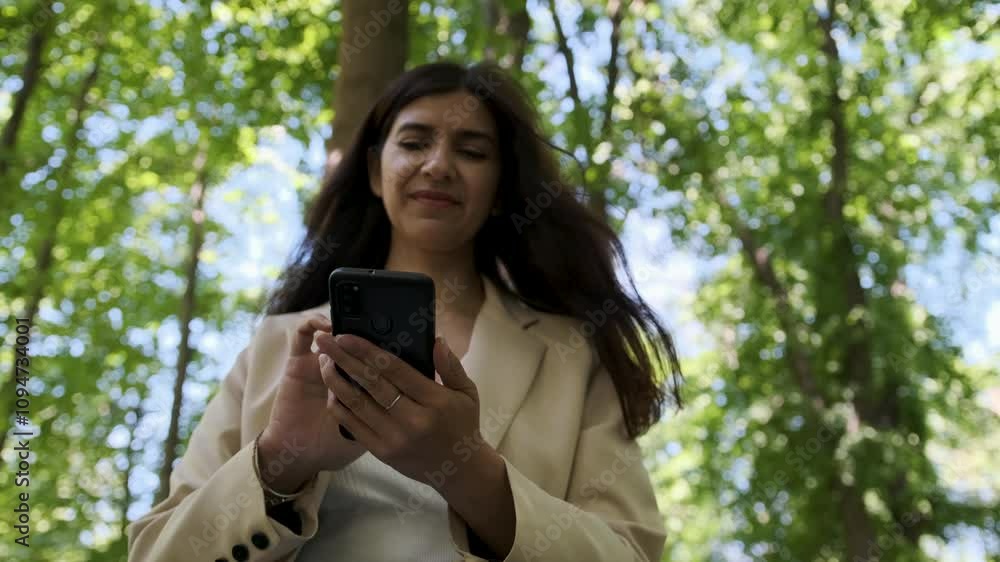 Businesswoman with long dark hair uses her smartphone in slow motion while surrounded by a serene green forest Businesswoman with long dark hair uses her smartphone in slow motion while surrounded by a serene green forest