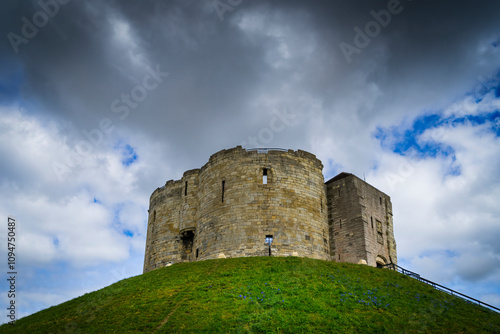 Ancient Clifford tower at dusk on a green hill and blue sky in the background with dark clouds. York City in the UK.