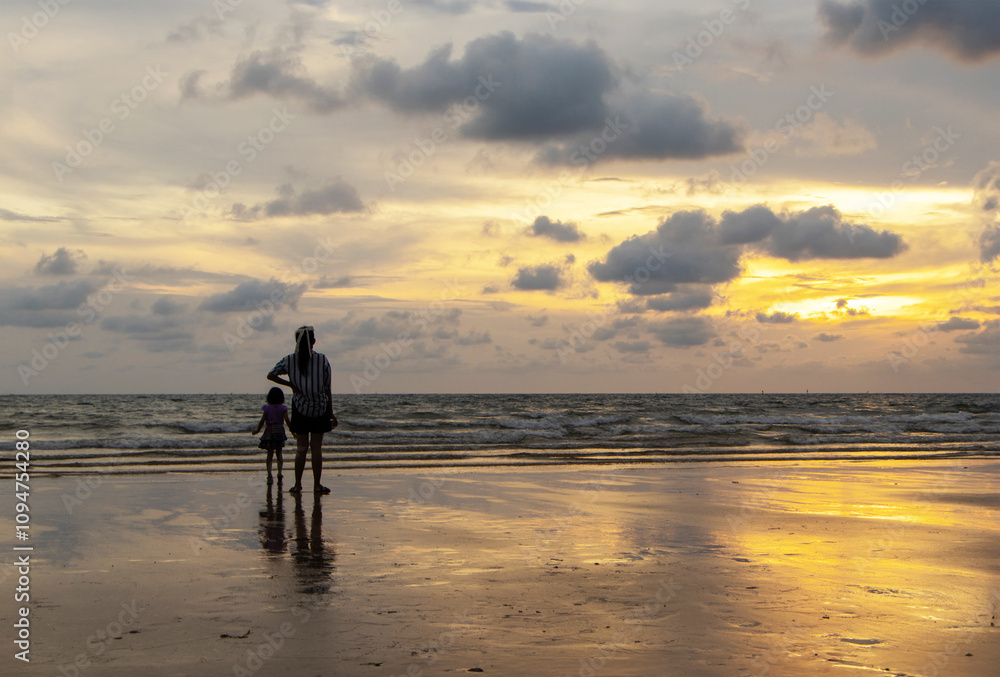 Naklejka premium Father and mother and children playing together outdoor on beach by sea. Happy family travel on beach in holiday, Summer vacations. Happy are having fun on a tropical beach in sunset and cloudy.