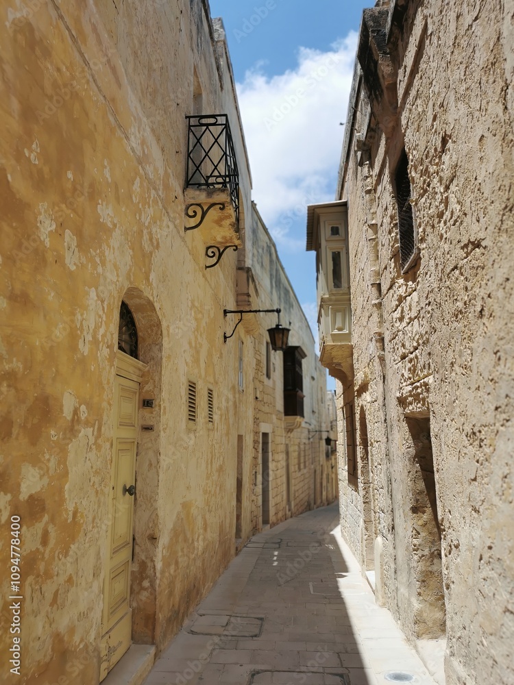 Obraz premium Narrow historic alleyway with rustic stone walls and traditional Maltese architecture in Mdina, Malta.