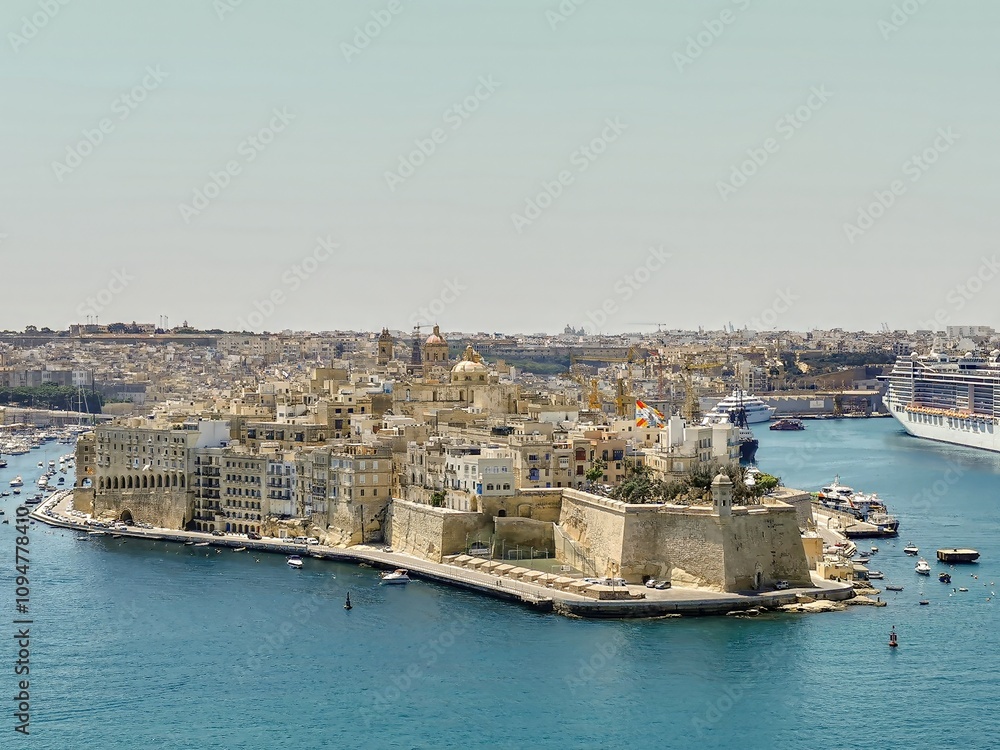 Fototapeta premium Aerial view of Senglea's historic fortified city, surrounded by the blue waters of the Grand Harbour, with ships and yachts nearby.