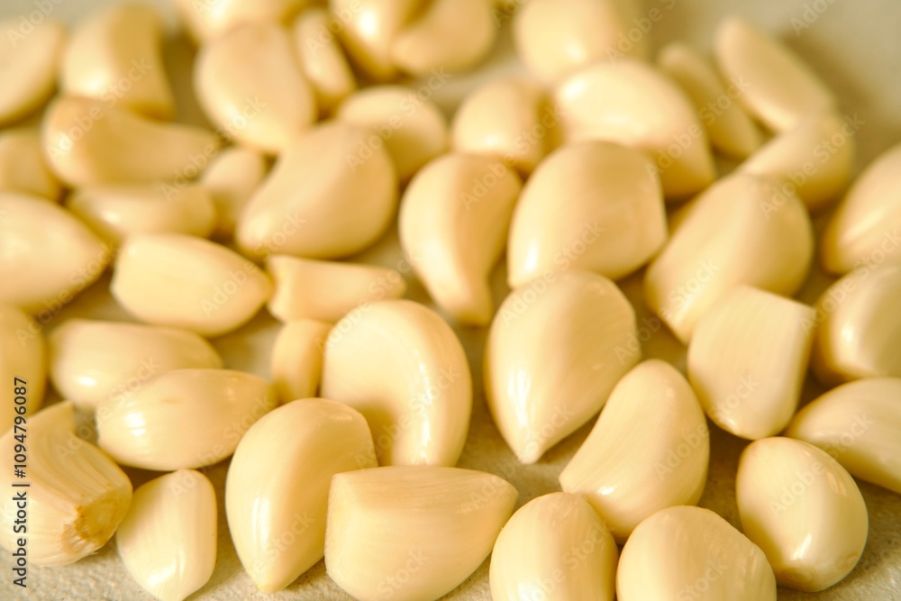 A pile of peeled garlic cloves spread out on a light textured surface, highlighting their smooth texture and natural color. A pile of peeled garlic cloves spread out on a light textured surface, highlighting their smooth texture and natural color.