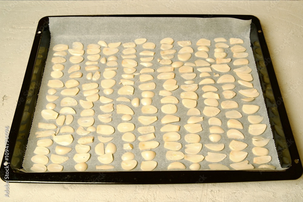Sliced garlic cloves neatly arranged on a baking tray lined with parchment paper, ready for drying or roasting. Sliced garlic cloves neatly arranged on a baking tray lined with parchment paper, ready for drying or roasting.