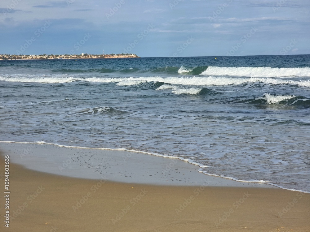 Aufnahme eines kleinen Küstenstreifens, wo die Wellen sanft auf den Sand treffen, das Meer sich ruhig erstreckt und der Horizont in der Ferne verschmilzt. Aufnahme eines kleinen Küstenstreifens, wo die Wellen sanft auf den Sand treffen, das Meer sich ruhig erstreckt und der Horizont in der Ferne verschmilzt.