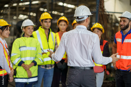group of diversity engineer factory worker standing in morning meeting with business man manager or executive boss leader team talking and brief in industry manufacturing warehouse. back or rear view