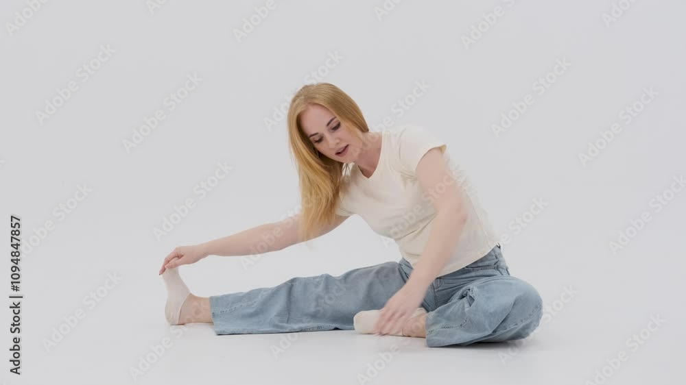 Young woman in casual clothing is performing a complete stretching routine on a white background Young woman in casual clothing is performing a complete stretching routine on a white background