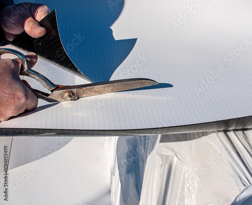 Construction worker cuts with large scissors a TPO polyolefin sheet to be applied for waterproofing a terrace of a new building photo