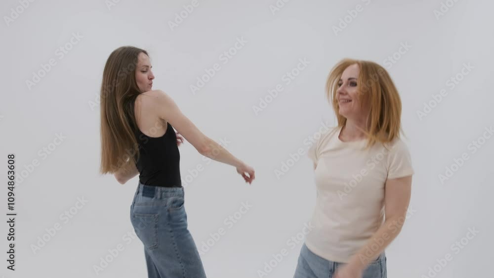 Two women joyfully dancing together in slow motion against a white background, showcasing fun and carefree movement Two women joyfully dancing together in slow motion against a white background, showcasing fun and carefree movement
